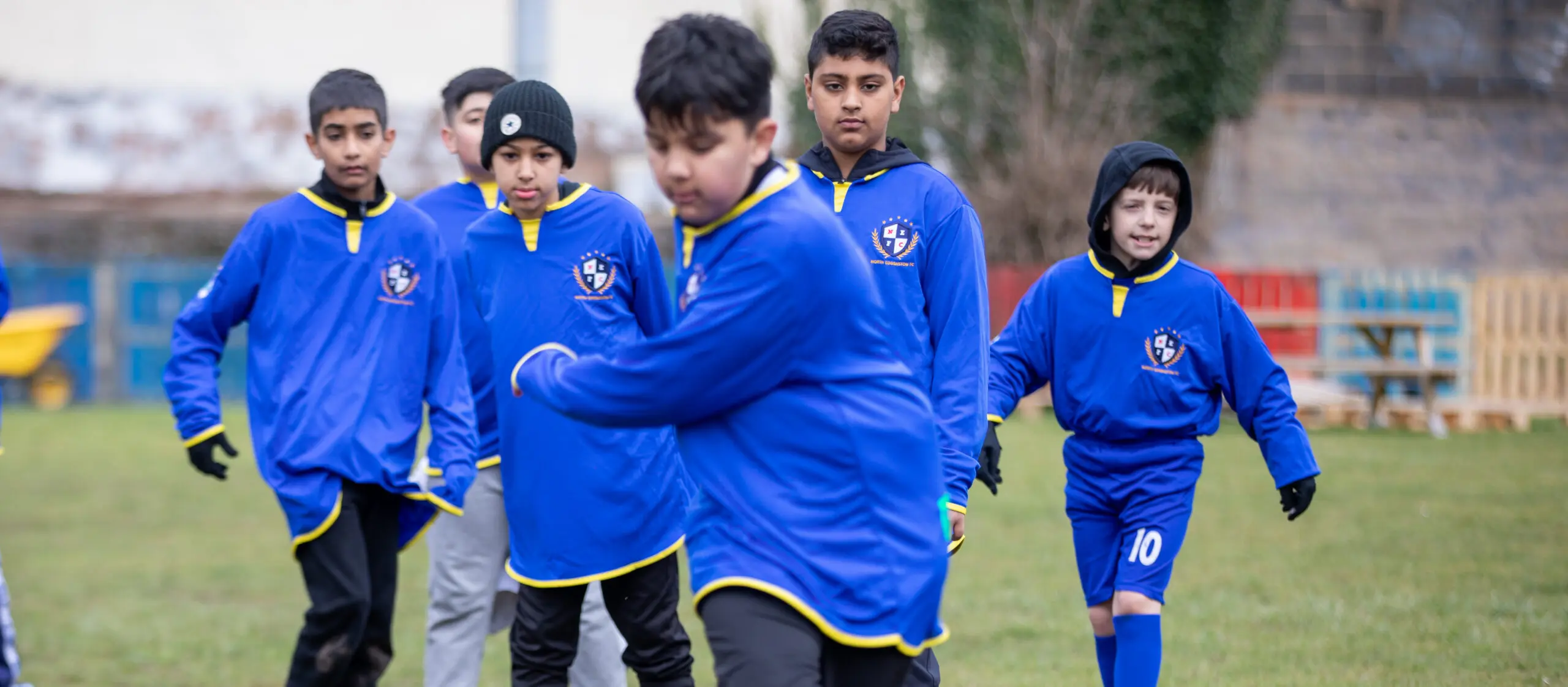 A group of young boys in blue football jerseys waiting on a grassy field, likely engaged in a football penalty shoot out.