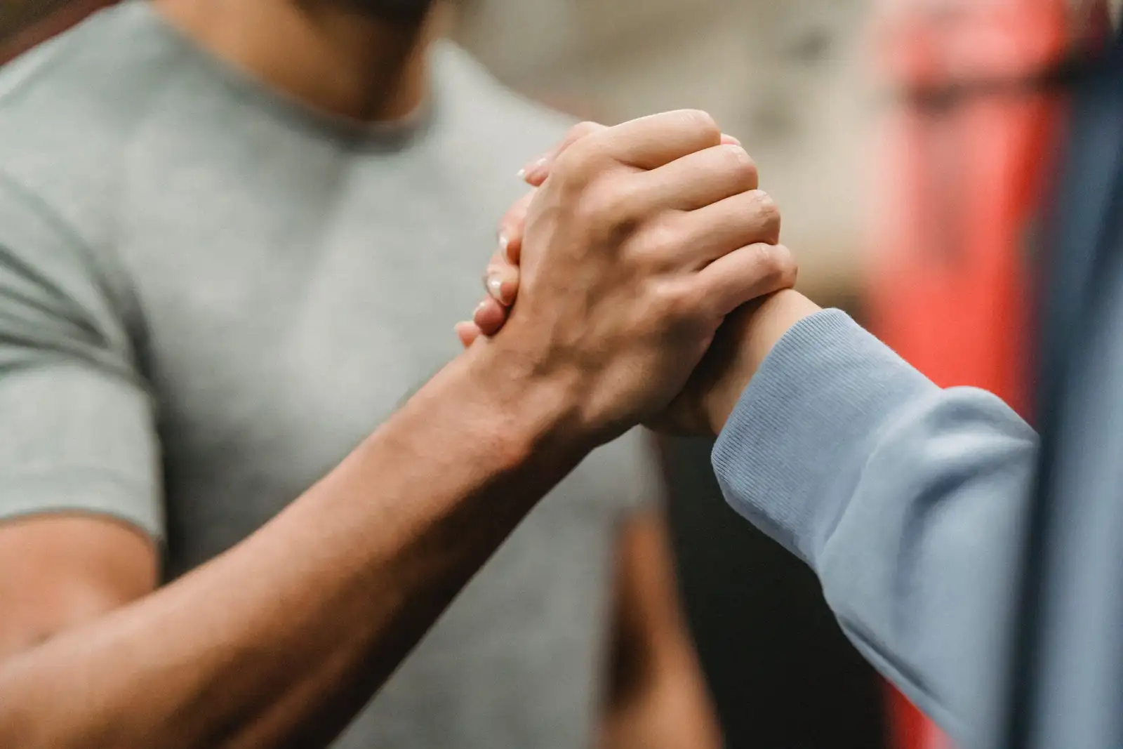 Two people joining hands together in a firm handshake or supportive clasp, symbolizing partnership, unity, and mutual support.